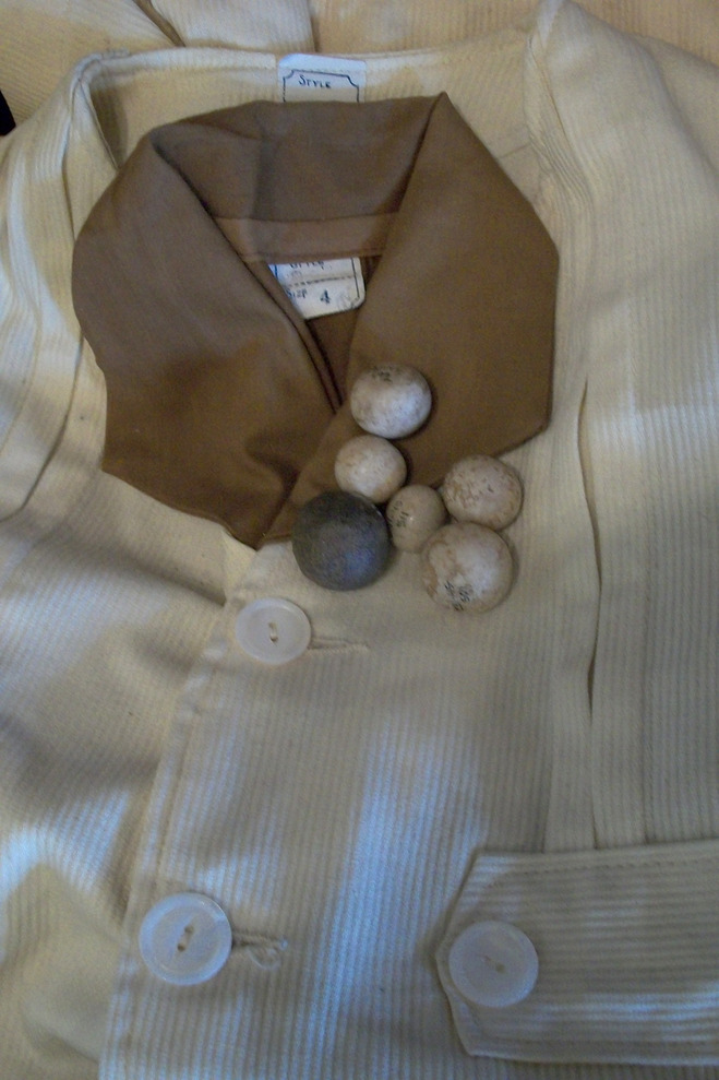 Six hand-formed clay marbles—one large speckled blue marble and five smaller mottled white marbles—rest upon the white corduroy jacket with the brown cotton collar, packed for travel in the suitcase on display at the Angel Island Immigration Station.