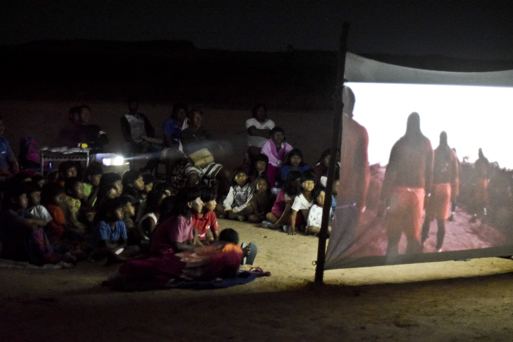 A photo of people watching a film projection outside at night